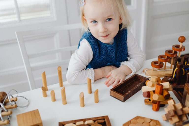 Young girl in white and blue outfit playing with wooden educational toys at a table indoors.