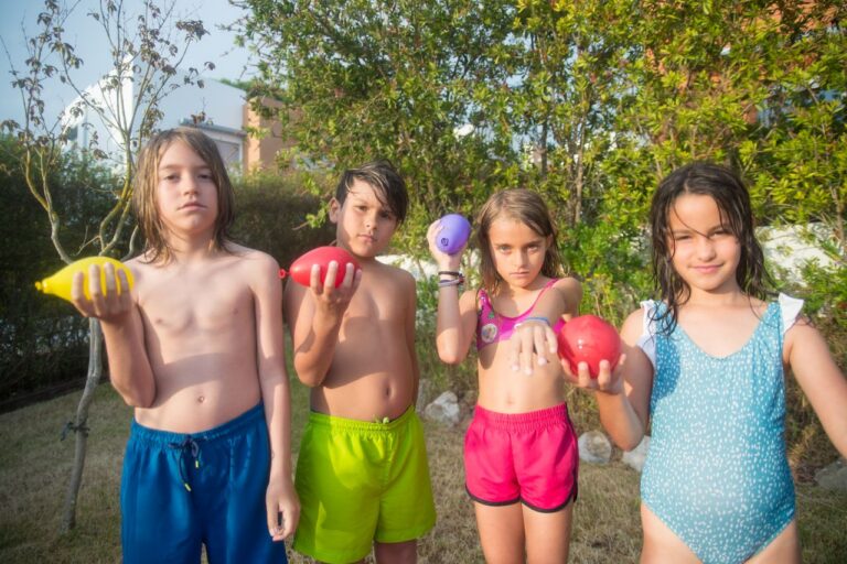 Four children holding colorful water balloons in a sunny garden setting.