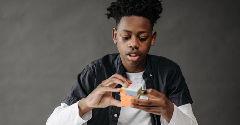 Young black teenager solving a Rubik's Cube in a studio setting on a gray background. - King Squishy - King Squishy