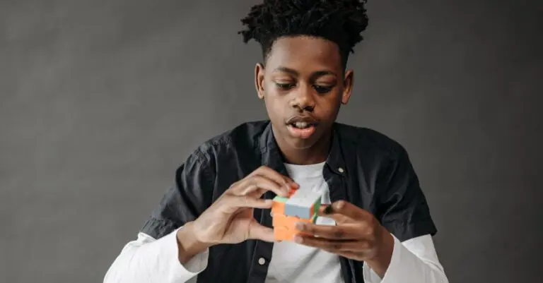 Young black teenager solving a Rubik's Cube in a studio setting on a gray background. - King Squishy - King Squishy