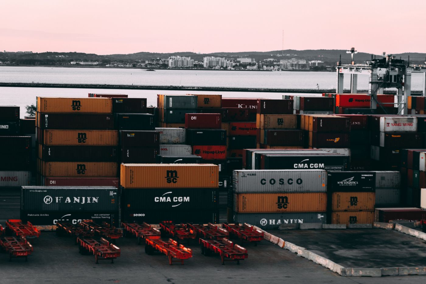 Ein geschäftiger Containerhof in einem Seehafen mit gestapelten, transportbereiten Schiffscontainern in der Abenddämmerung.