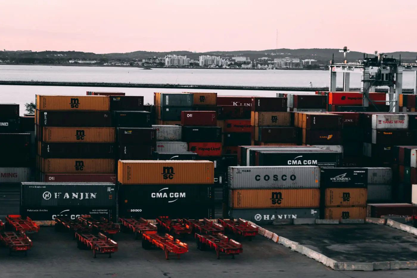 Un vivace piazzale di container in un porto marittimo con container di spedizione impilati e pronti per il trasporto al tramonto.