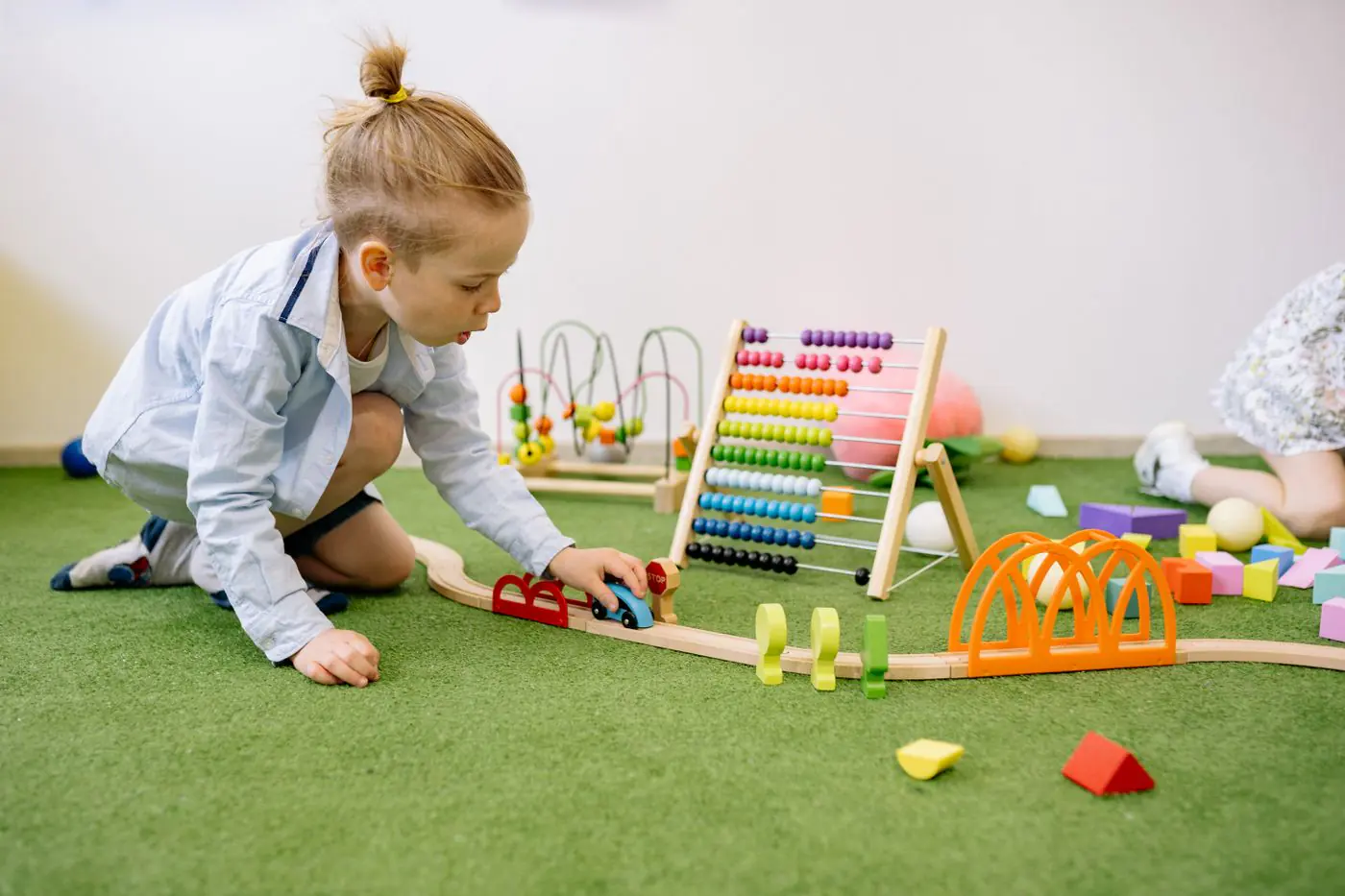 Young child playing with colorful educational toys indoors on a green carpet. - King Squishy