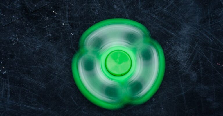 A vibrant green fidget spinner spinning rapidly against a dark textured background. - King Squishy