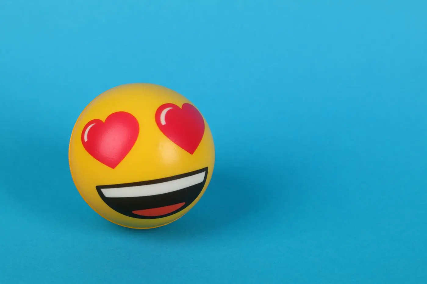 A cheerful heart eyes emoji stress ball resting on a vibrant blue background, symbolizing love and joy.