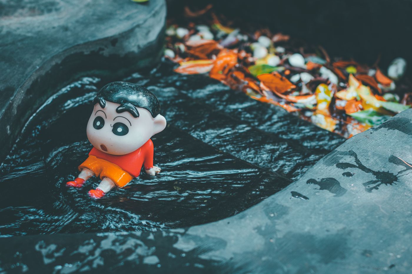 Spielzeugfigur einer Zeichentrickfigur in einem dunklen Wasserlauf, umgeben von gefallenen Blättern.