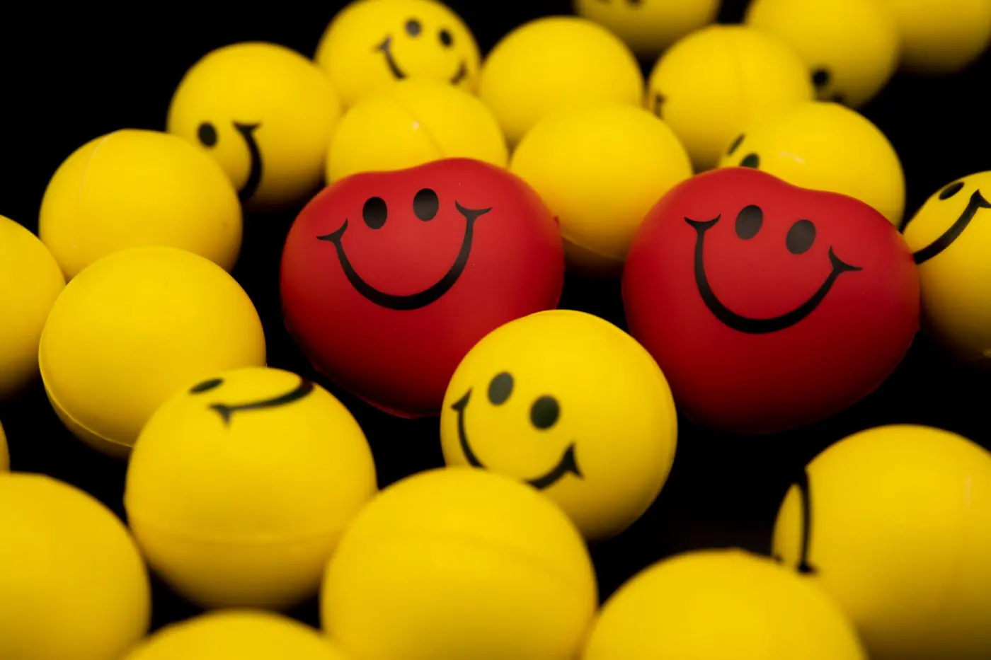 Bright collection of yellow and red smiley face balls and hearts on a dark background. - King Squishy