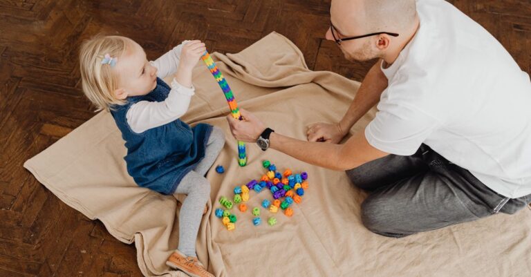 Father and young daughter bonding over a playful activity with colorful blocks on a wooden floor. - King Squishy