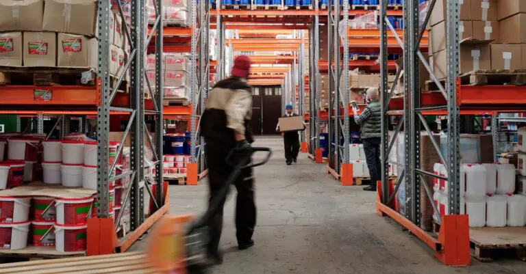Warehouse interior with workers organizing shelves full of boxes and containers. - King Squishy - King Squishy