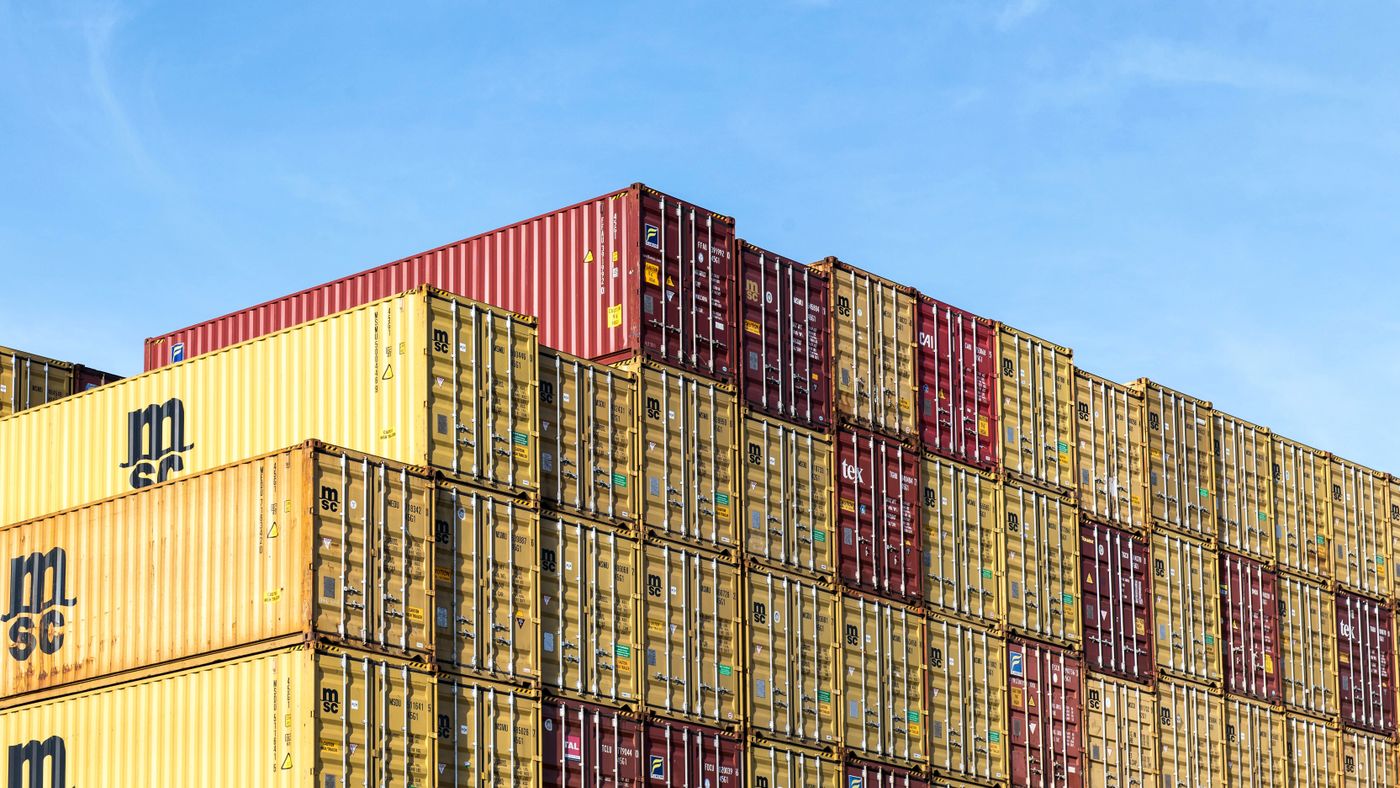 Conteneurs de fret colorés empilés dans le port de Hambourg sous un ciel bleu dégagé.