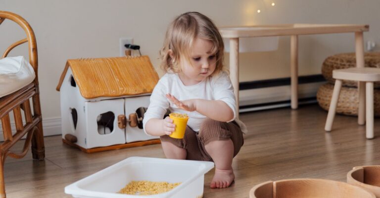 A young child playing with macaroni in a cozy indoor playroom setting. - King Squishy