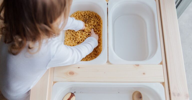 Curious child engaging in sensory play with pasta, exploring textures indoors. - King Squishy