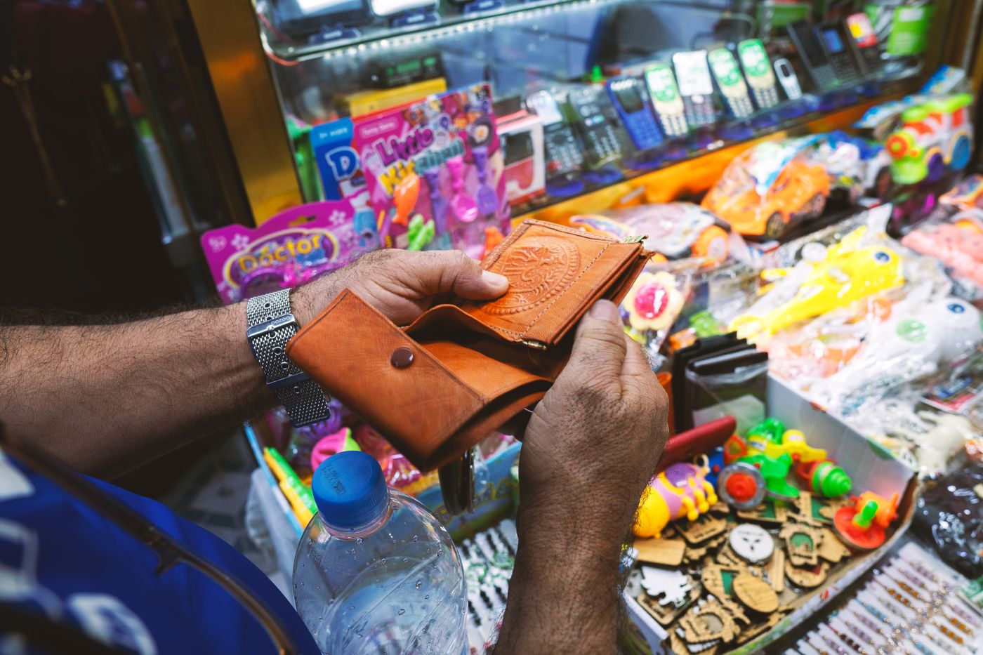 Une personne tenant un portefeuille en cuir près d'un stand de jouets colorés dans un marché animé. - King Squishy