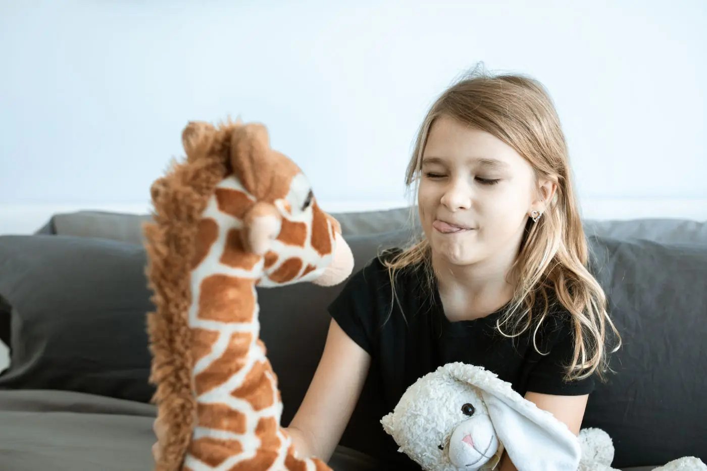 A young girl joyfully interacts with stuffed animals in a cozy indoor setting, showcasing playful childhood moments. - King Squishy
