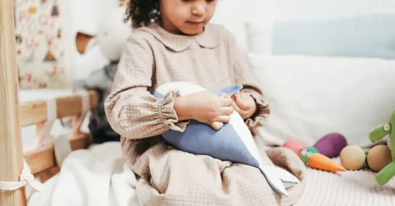 A young girl in a brown dress holds a whale plush toy, surrounded by colorful stuffed animals i - Ki - King Squishy