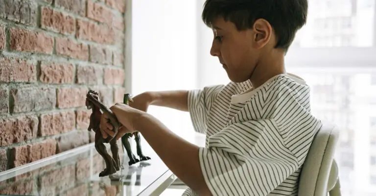 A young boy playing with dinosaur figures against a brick wall in a well-lit room. - King Squishy
