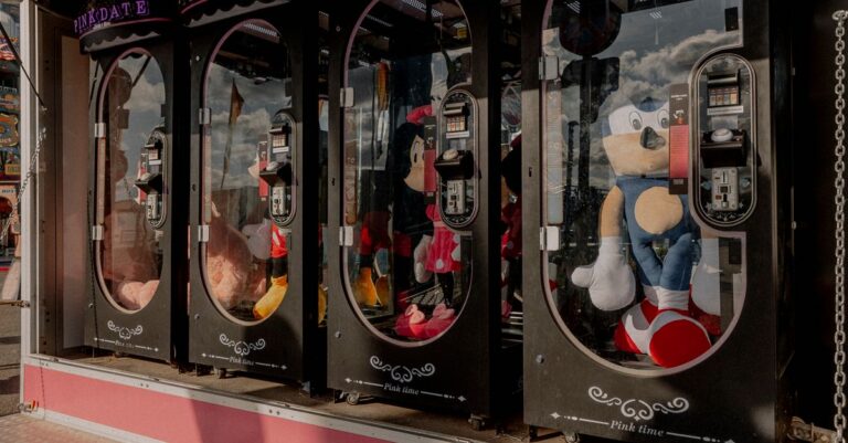 Colorful claw machines filled with plush toys at a fairground arcade, reflecting a fun atmosphe - Ki - King Squishy