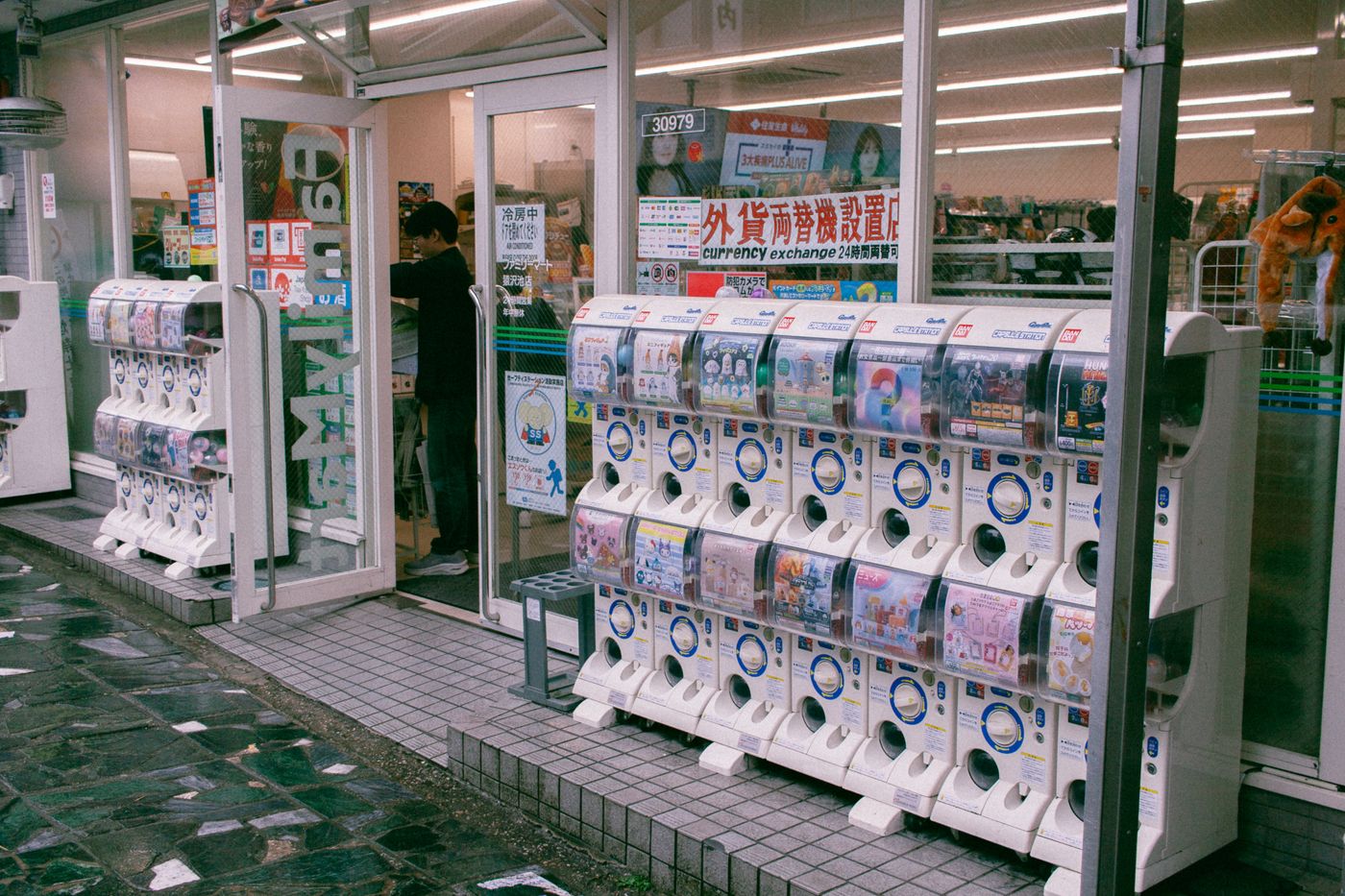 Reihen von Gashapon-Verkaufsautomaten vor einem japanischen Geschäft, die Spielzeugkapseln anbieten. - King Squishy