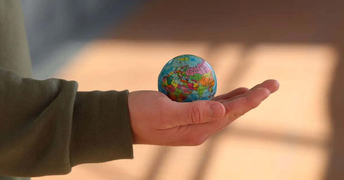 Close-up of a hand holding a small globe with blurred background, emphasizing depth and exploration. - King Squishy