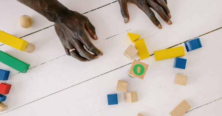 Hands playing with colorful wooden blocks on a white table, sparking creativity and learning. - King Squishy
