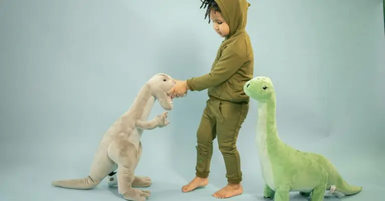 Side view full body of little curious African American boy in green dinosaur costume playing wi - Ki - King Squishy