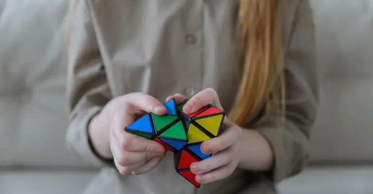 Crop anonymous girl demonstrating and solving colorful puzzle with triangles in soft focus - King Squishy