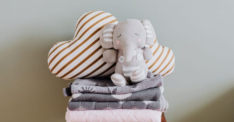 Cute elephant toy on cozy blankets with a heart pillow, perfect for baby room decor. - King Squishy - King Squishy