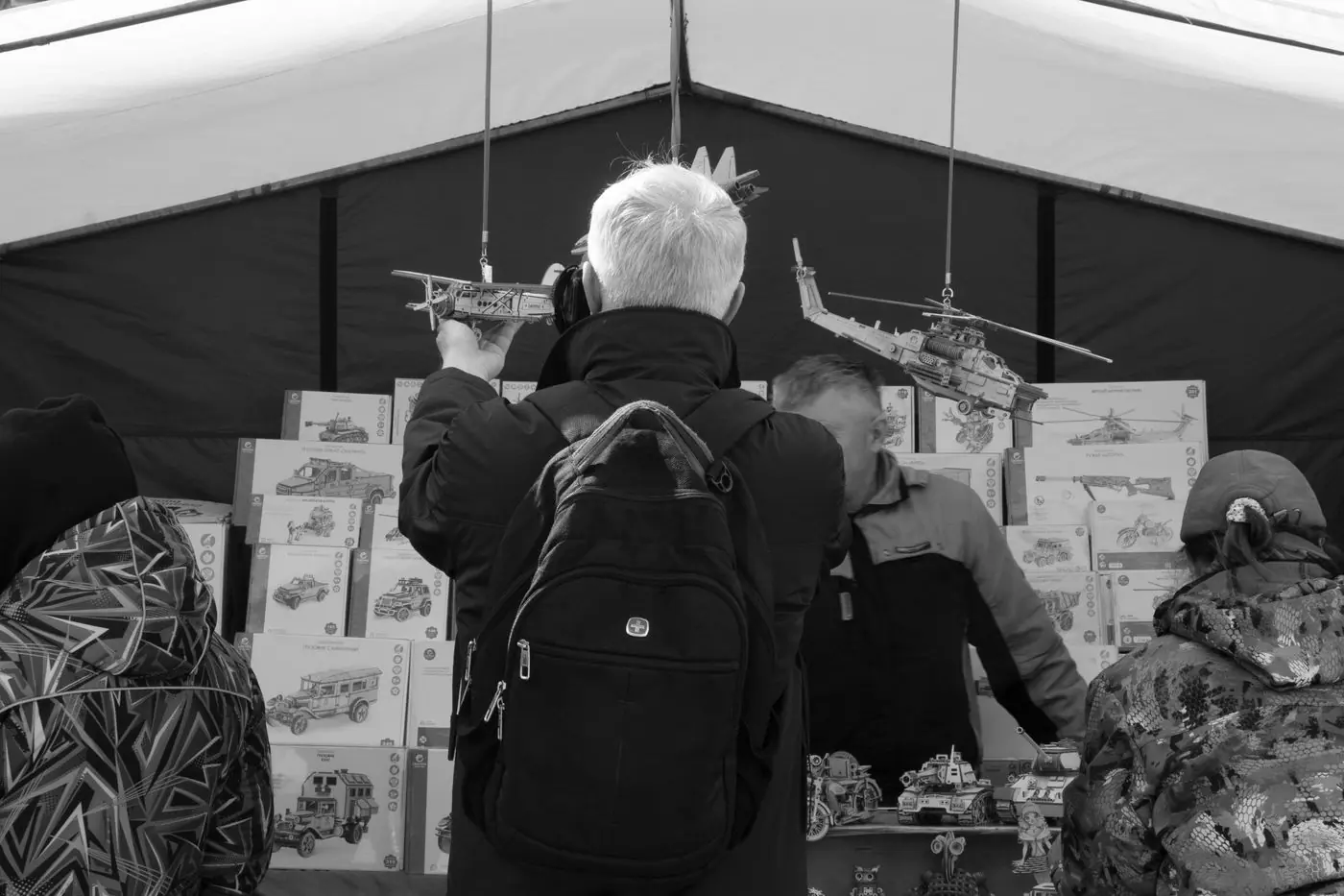 Adult browsing toy helicopters at a market stall, captured in black and white for a candid feel. - King Squishy