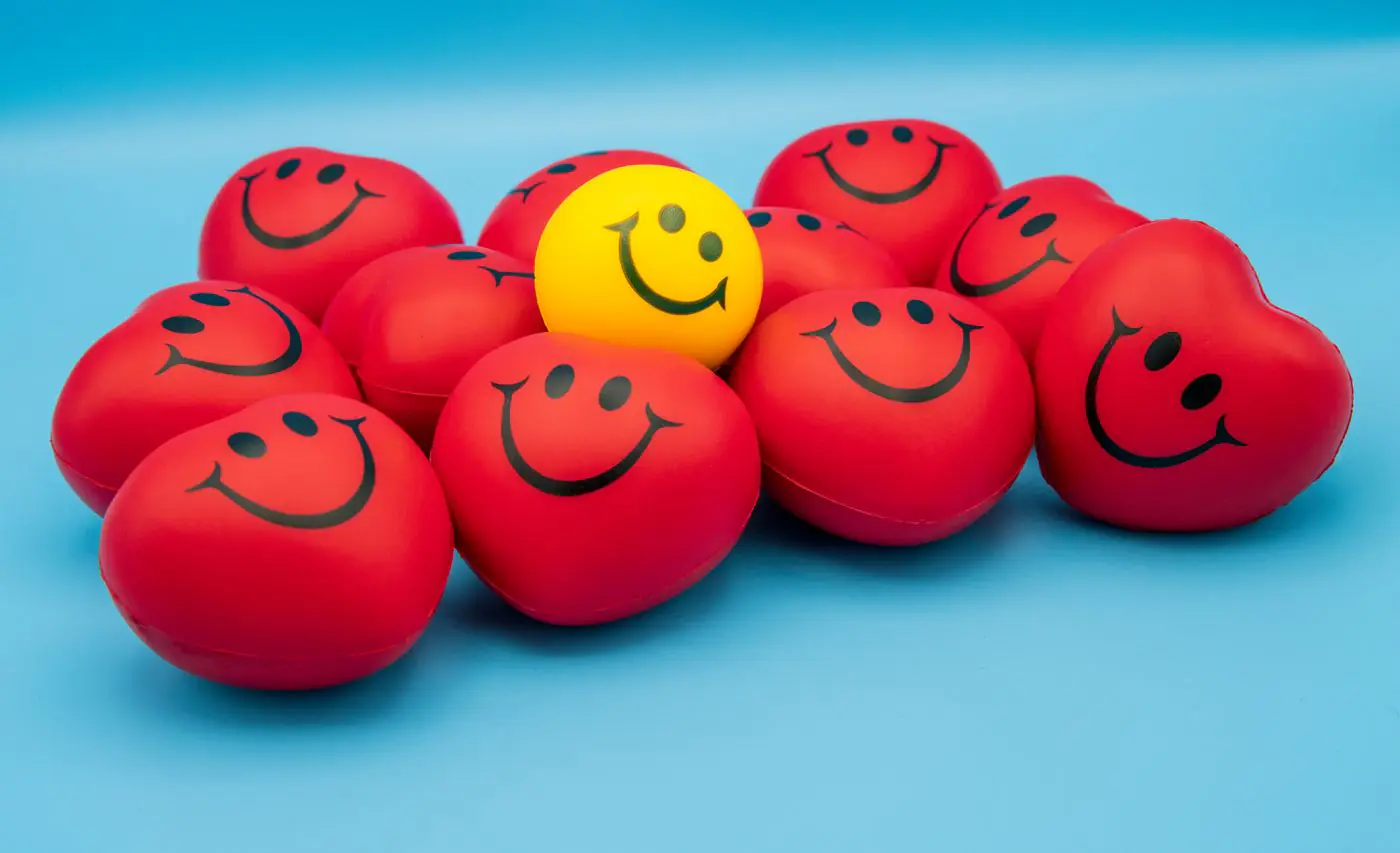 Heart-shaped red and yellow smiley stress balls on a blue surface conveying positivity and stress relief. - King Squishy