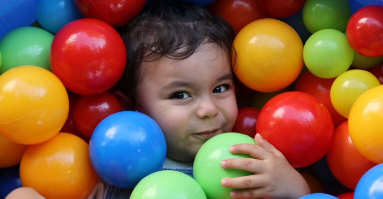 Adorable child smiling and playing in a vibrant ball pit indoors. - King Squishy - King Squishy