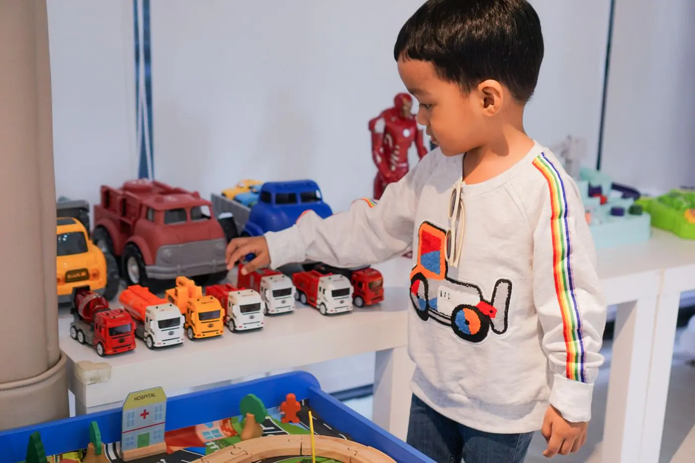 A young boy playing indoors with colorful toy trucks on a table, focused and imaginative. - King Squishy
