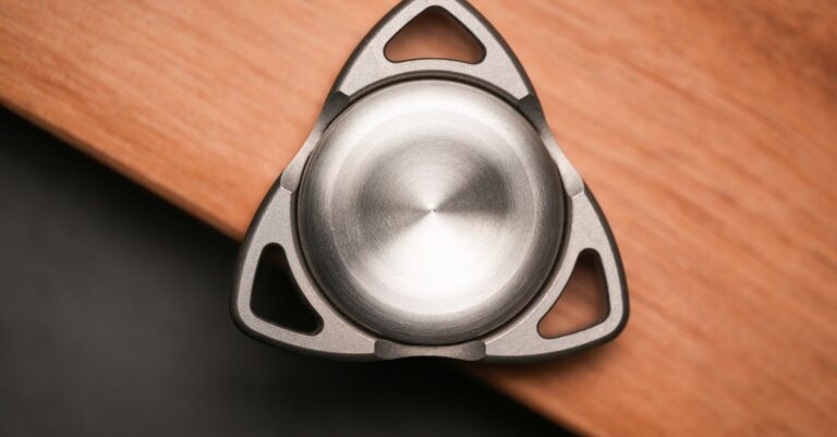 Close-up of a metallic fidget spinner on a wooden table, showcasing its design and texture. - King Squishy