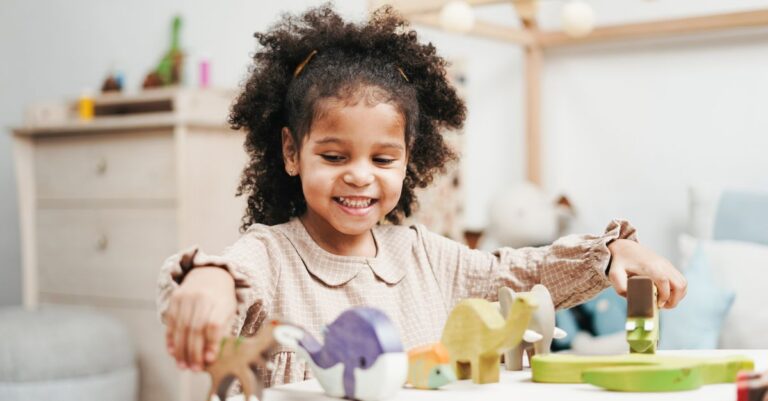 A joyful girl playing with colorful wooden toys at a table in a bright playroom. - King Squishy
