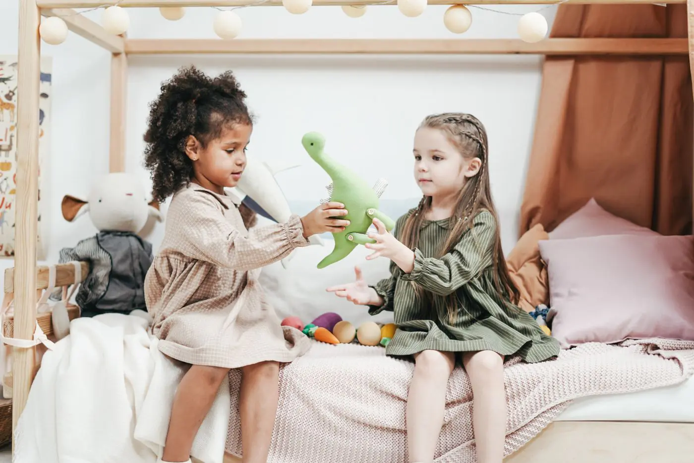 Dua Anak Perempuan Muda Berbagi Boneka Dinosaur Plush Sambil Duduk di Tempat Tidur di Kamar Bermain yang Nyaman. - King Squishy