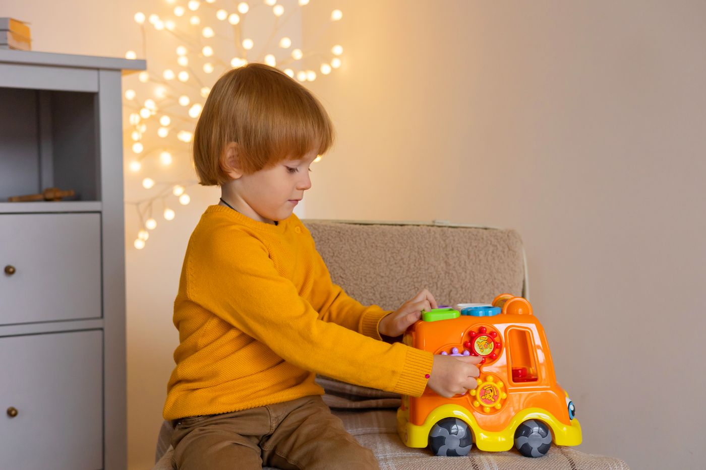 Un niño pequeño disfruta jugando con un camión de juguete colorido en interiores, rodeado de luces cálidas. - King Squishy