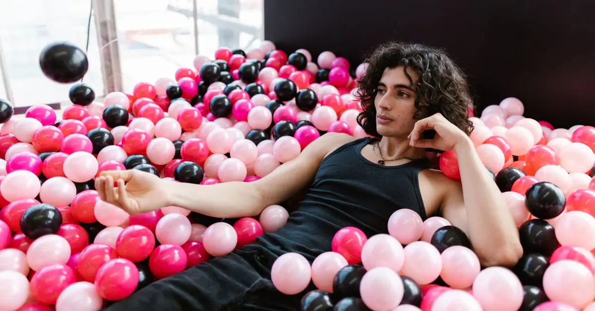 Portrait of a young man lounging amidst colorful plastic balls in an indoor setting. - King Squishy
