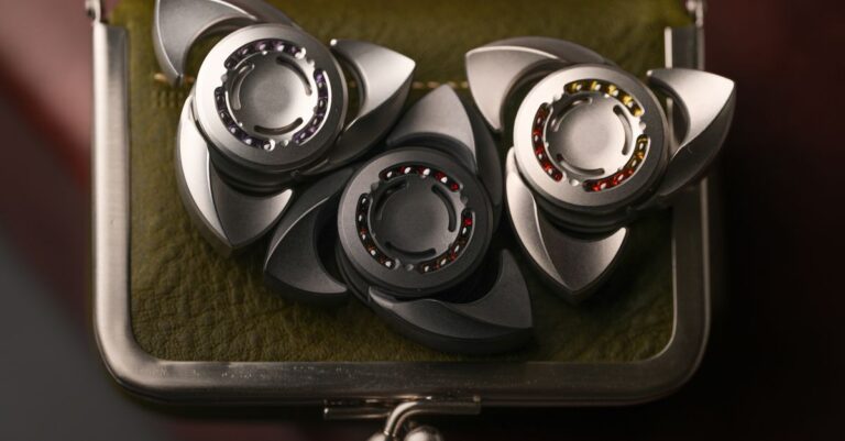 Three metallic fidget spinners elegantly displayed on a leather case under warm lighting. - King Squishy