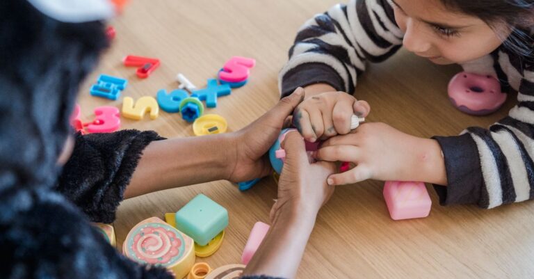Two children in animal costumes play with colorful toys on a wooden table. - King Squishy
