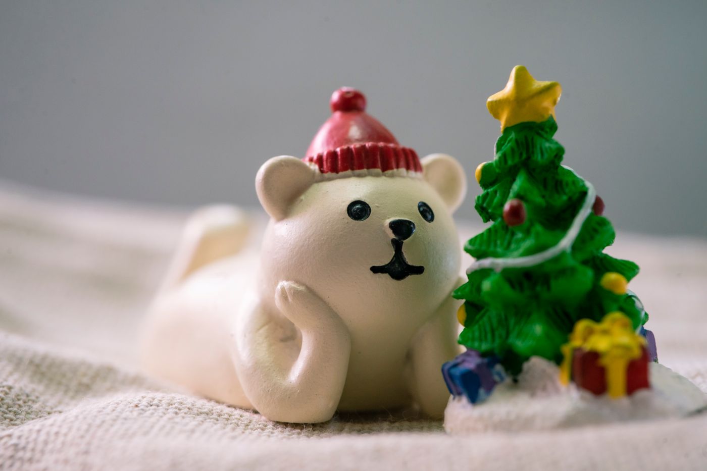 Nahaufnahme einer Bärenfigur und eines Weihnachtsbaums mit Geschenken, die festliche Stimmung einfängt. - King Squishy