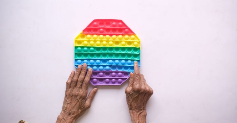 Close-up of elderly hands on a rainbow silicon push popper toy on white background. - King Squishy