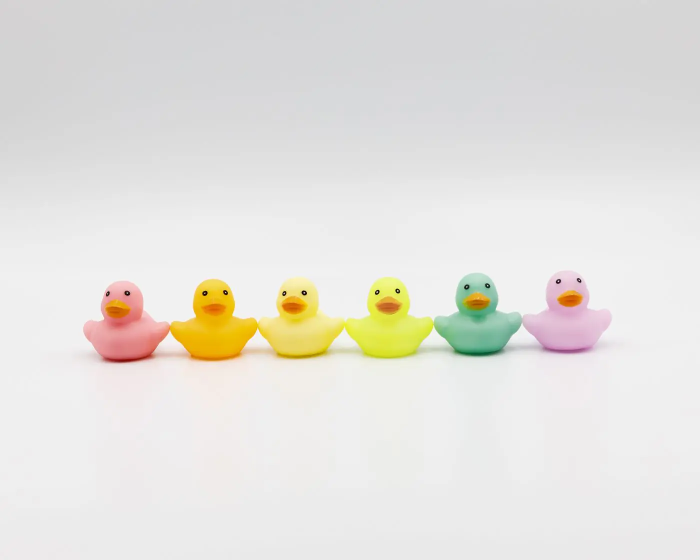 Lebendige, bunte Gummienten in einer Reihe auf sauberem weißem Hintergrund. - King Squishy