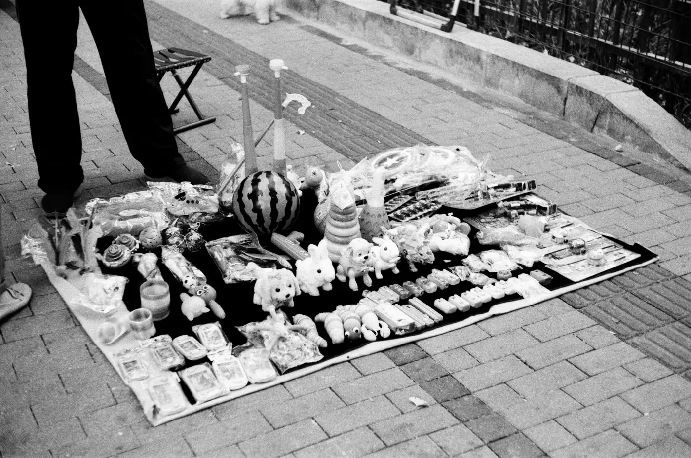 Foto hitam putih mainan yang dijual di atas tikar oleh pedagang kaki lima di pasar perkotaan. - King Squishy