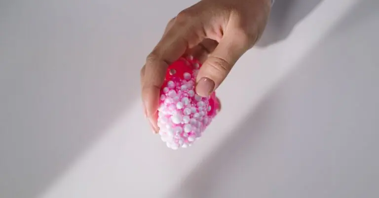 A hand gently holds a pink textured slime with small foam beads, showcasing tactile sensation. - King Squishy