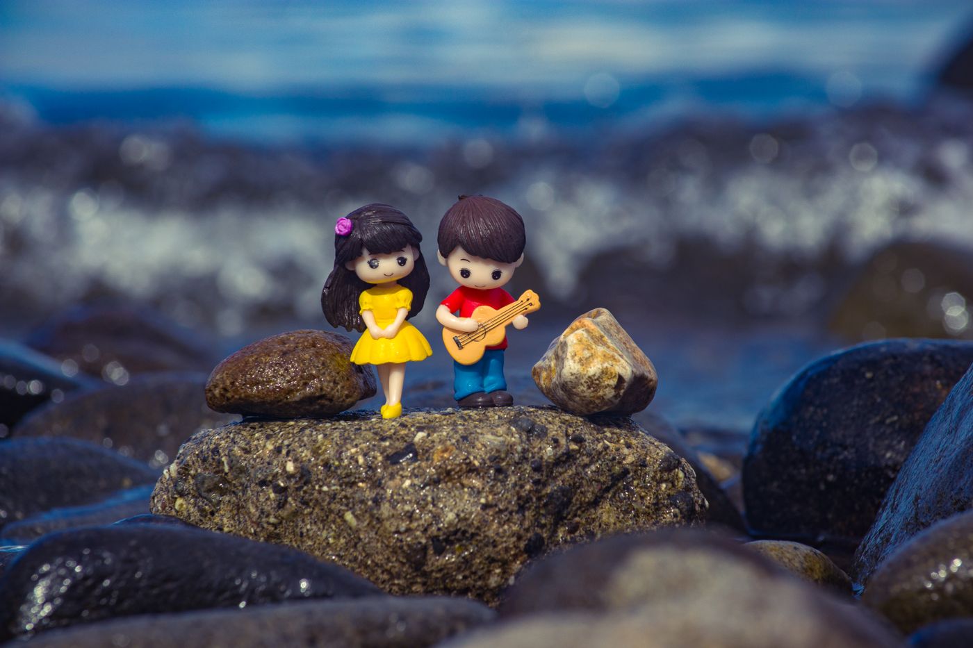 Un par de figuras en miniatura sobre una roca cubierta de musgo junto a la orilla del mar, representando una escena lúdica. - King Squishy