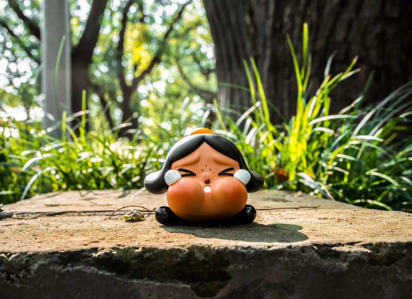 Adorable cartoon figurine on a stone surrounded by lush green grass in sunlight.