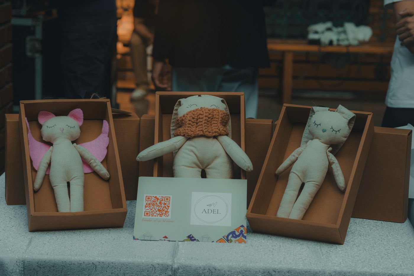 A close-up of handmade plush toys in cardboard boxes displayed indoors at a craft event. - King Squishy