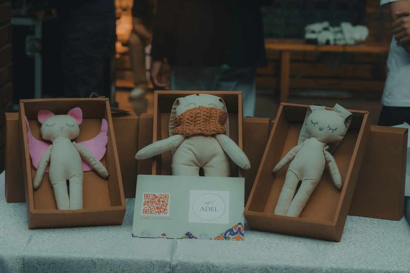 A close-up of handmade plush toys in cardboard boxes displayed indoors at a craft event. - King Squishy