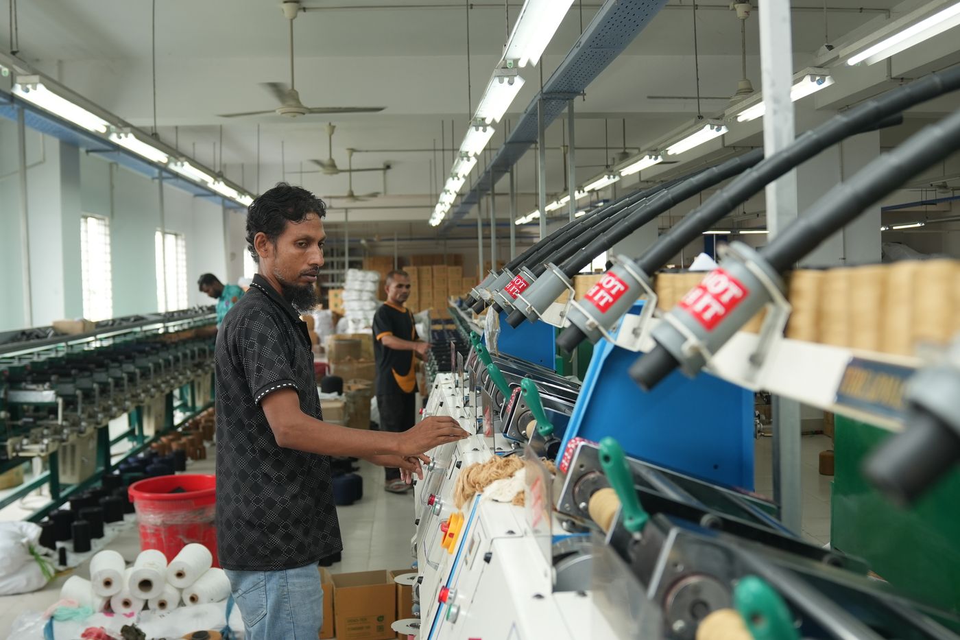 Trabajador operando maquinaria textil en una fábrica, centrándose en la eficiencia de la producción.